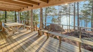 Eine Holzterrasse mit Tisch und Bänken mit Blick auf einen von Bäumen umgebenen See.