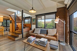 A modern living room with a staircase, leather sofa, books, and large windows with a view. - Stylish unquie beach side property with all amenities (Surf Beach)