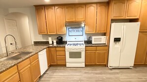 A kitchen with wooden cabinets, a white stove, a microwave, and a refrigerator. - Ocotillo Wells Paradise. The best off-road hose in Ocotillo Wells. (Thermal)