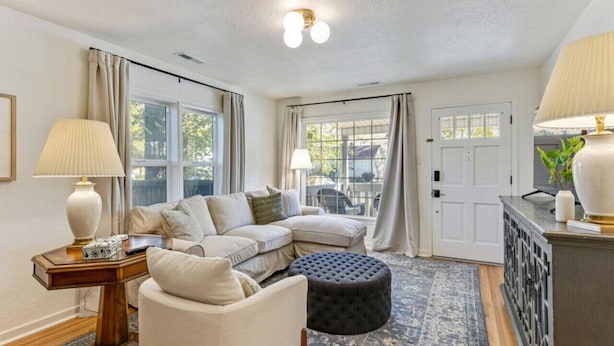A living room with a sectional sofa, a round ottoman, a side table, and a lamp. - Luxe Mountainview Haven | Backyard | Massage* (Provo)
