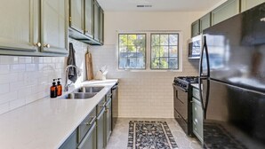 A kitchen with light green cabinets, a stainless steel refrigerator, a gas stove, and a window providing natural light. - Luxe Mountainview Haven | Backyard | Massage* (Provo)