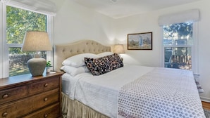 A bedroom with a large bed, a nightstand, a lamp, a window with a view of trees, and a framed picture on the wall. - Luxe Mountainview Haven | Backyard | Massage* (Provo)
