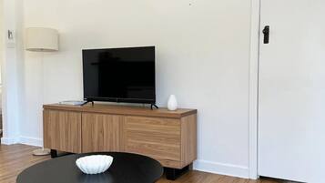 Una sala de estar moderna con una televisión de pantalla plana sobre un mueble de madera, una mesa redonda negra con un cuenco blanco y una lámpara de pie.