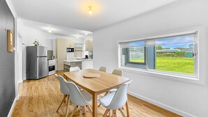 A modern kitchen with a dining area, wooden flooring, and a large window with a view of a green landscape.