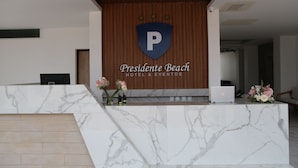 Un comptoir d’accueil d’hôtel avec un revêtement en marbre, un mur recouvert de panneaux en bois et un logo représentant un écu et la lettre « P ».