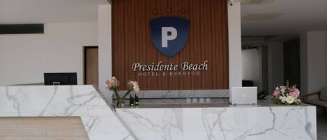 A hotel reception desk with a marble counter, a wooden panel wall, and a logo with a shield and a 'P'.