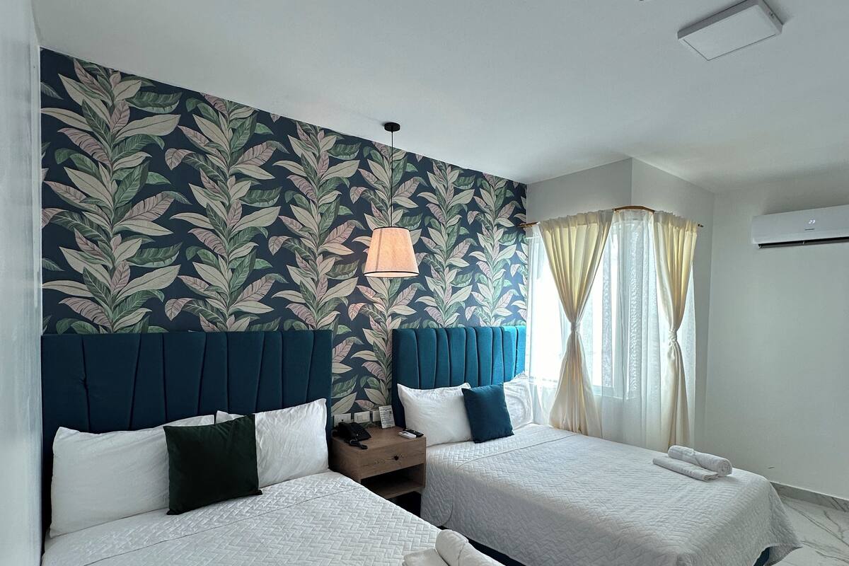 Ein Hotelzimmer mit zwei Betten, einem Nachttisch, einer Lampe, einer Deckenleuchte und einem Fenster mit Vorhängen.