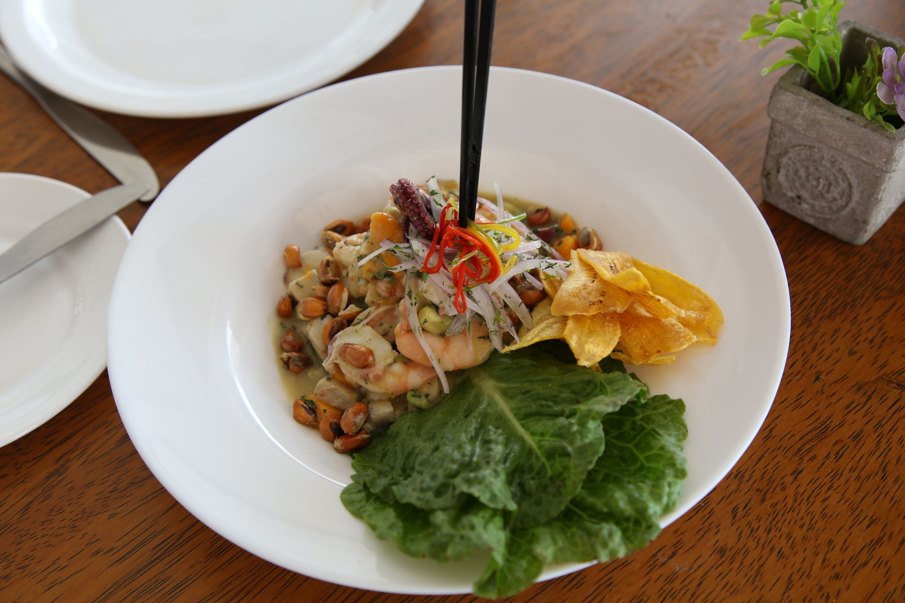 A white plate with a seafood dish, including shrimp and peanuts, on a wooden table.