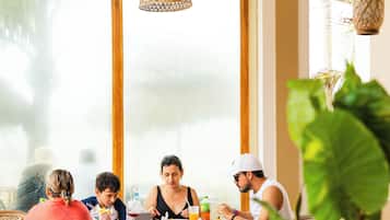 Un espace repas avec des chaises en osier, de grandes fenêtres et des luminaires suspendus en fibres tressées.