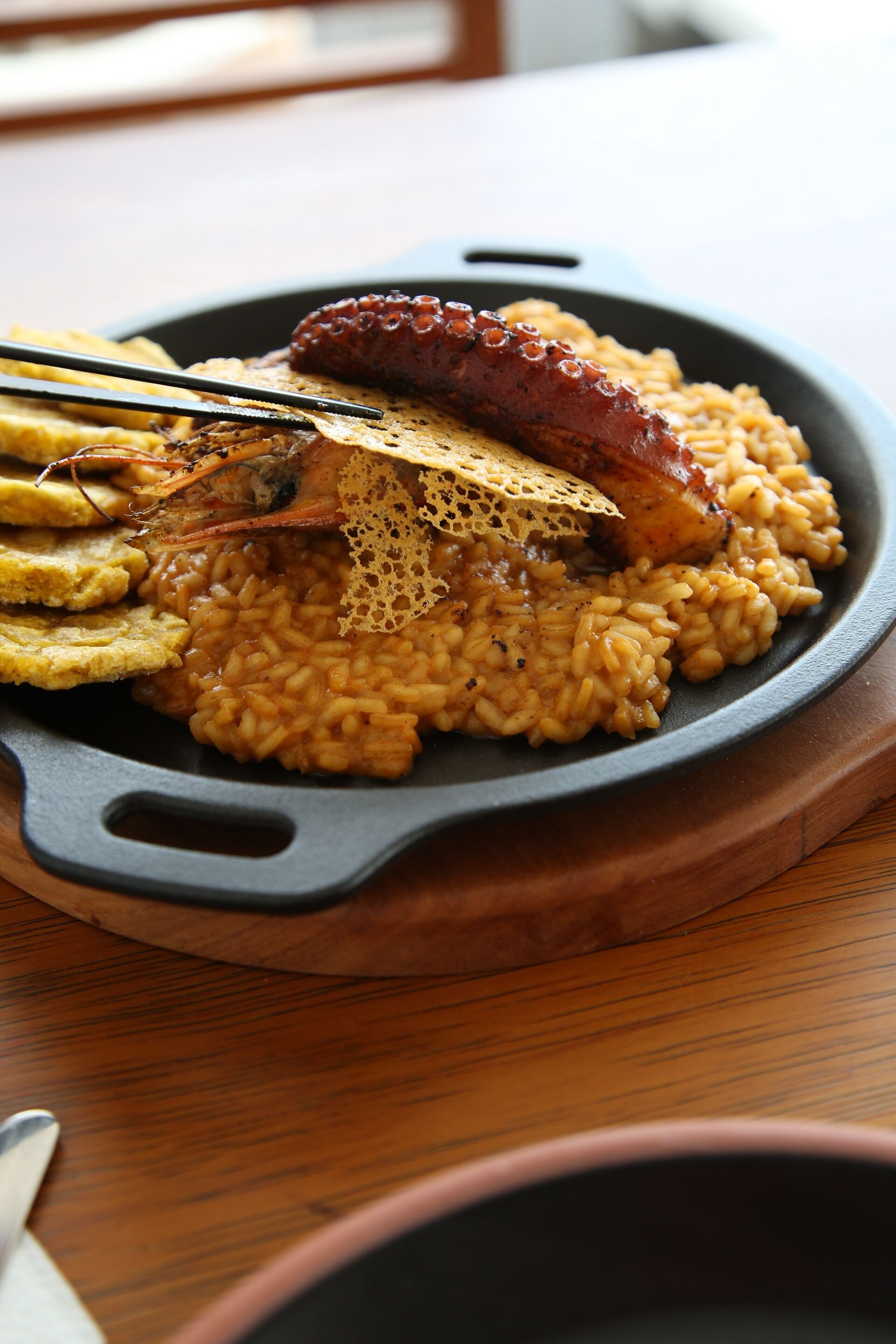 A plate of food with rice, a sausage, and plantains on a black skillet.