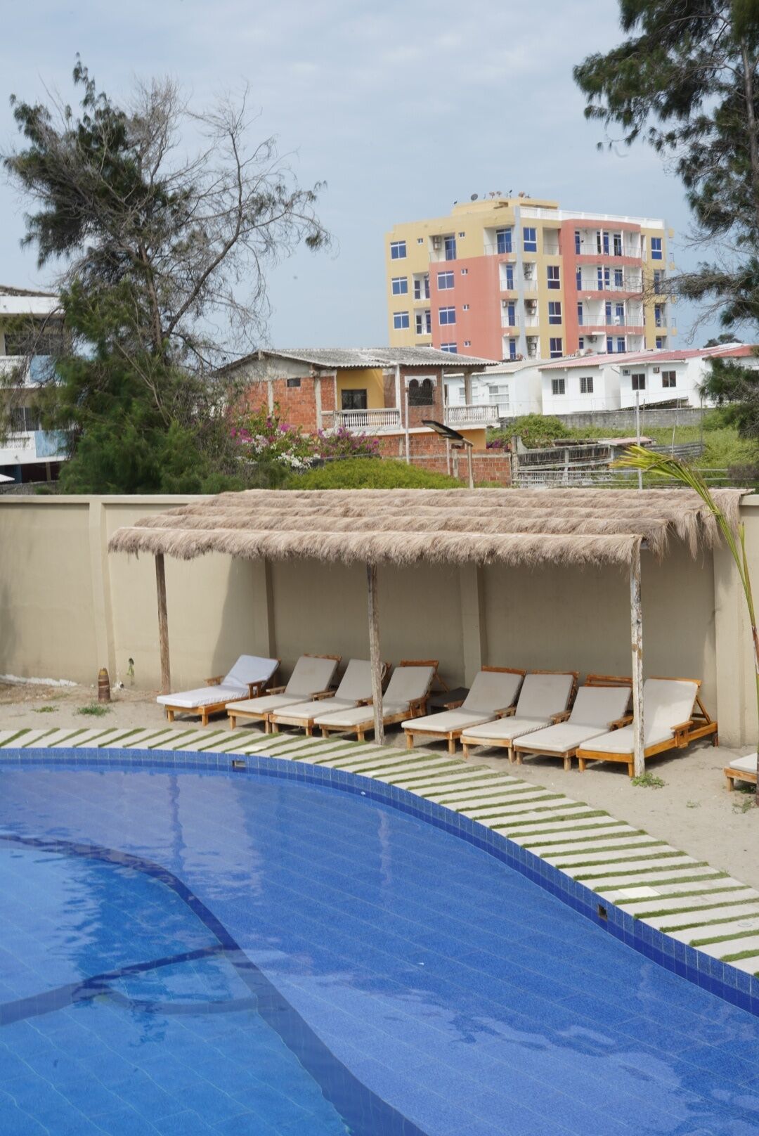 Una piscina con sillones de descanso y una estructura de techo de paja.