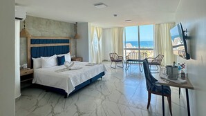 Une chambre d’hôtel avec un lit, une table à manger avec des chaises, une télévision et une vue sur la plage.