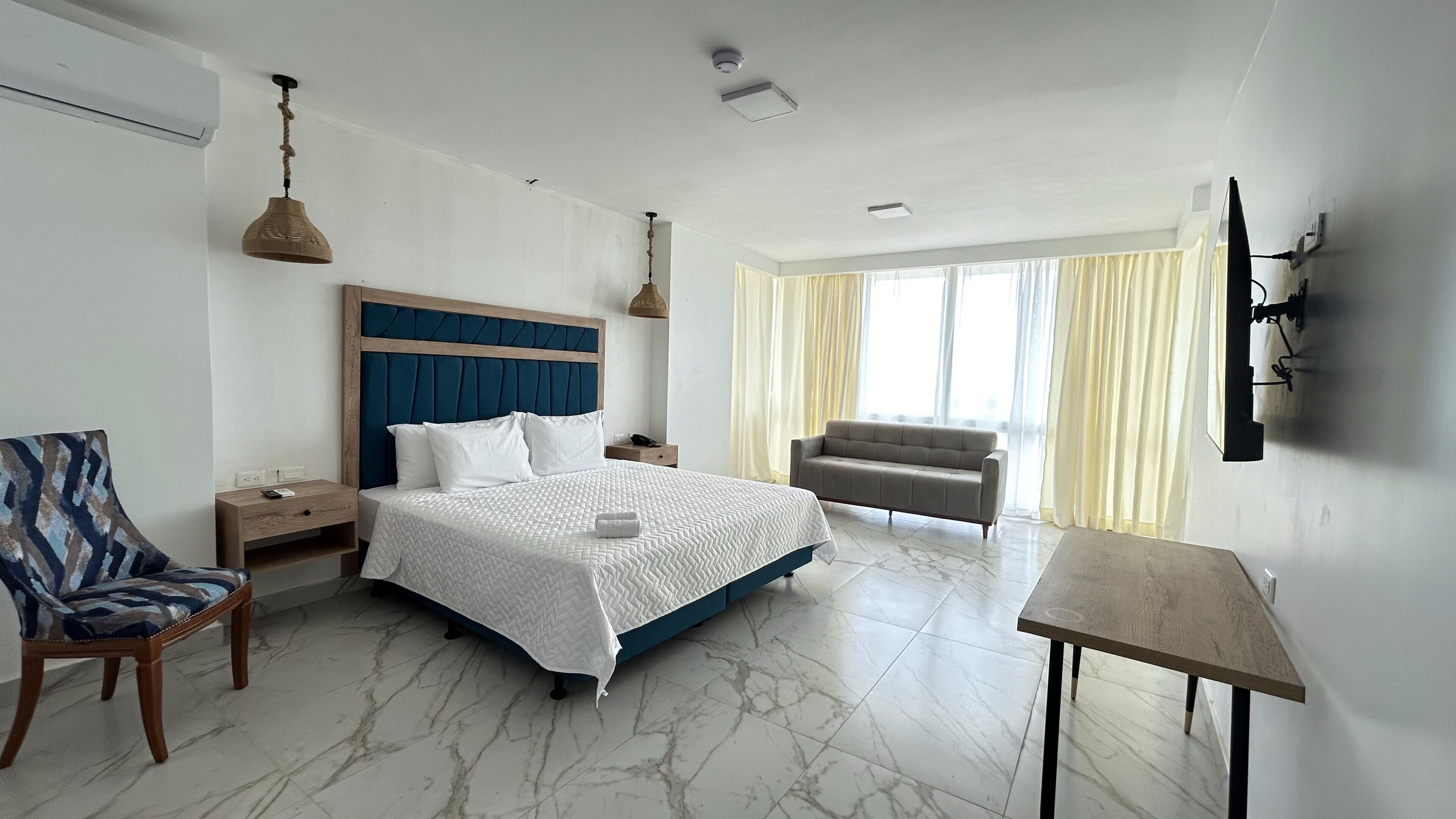 A hotel room with a bed, a chair, a table, and a TV mounted on the wall.