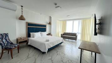 A hotel room with a bed, a chair, a table, and a TV mounted on the wall.