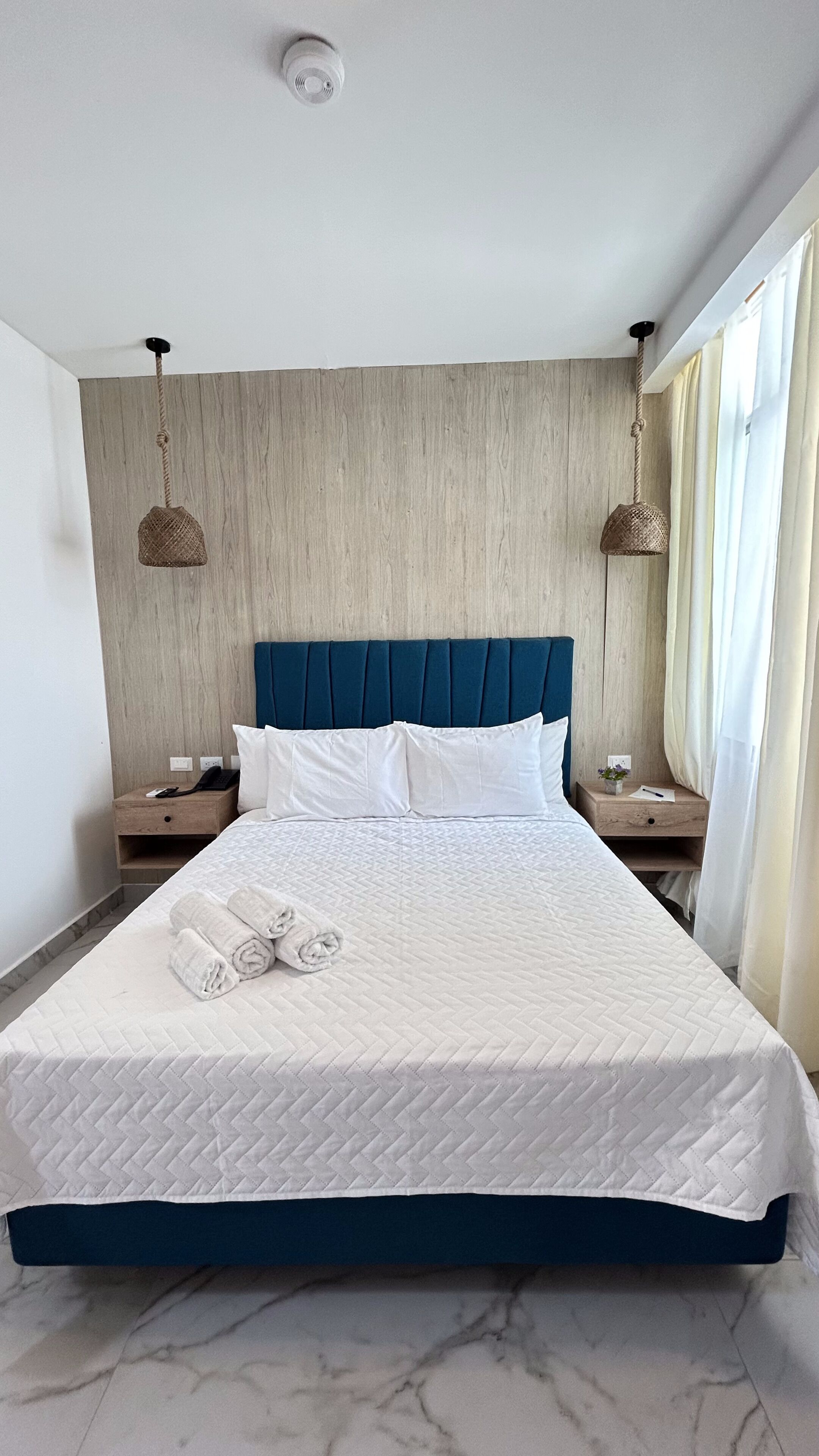 A neatly made bed with a quilted white duvet, a blue upholstered headboard, and two bedside tables with lamps.