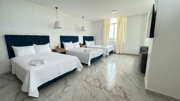 A hotel room with three beds, a marble floor, and a TV on the wall.