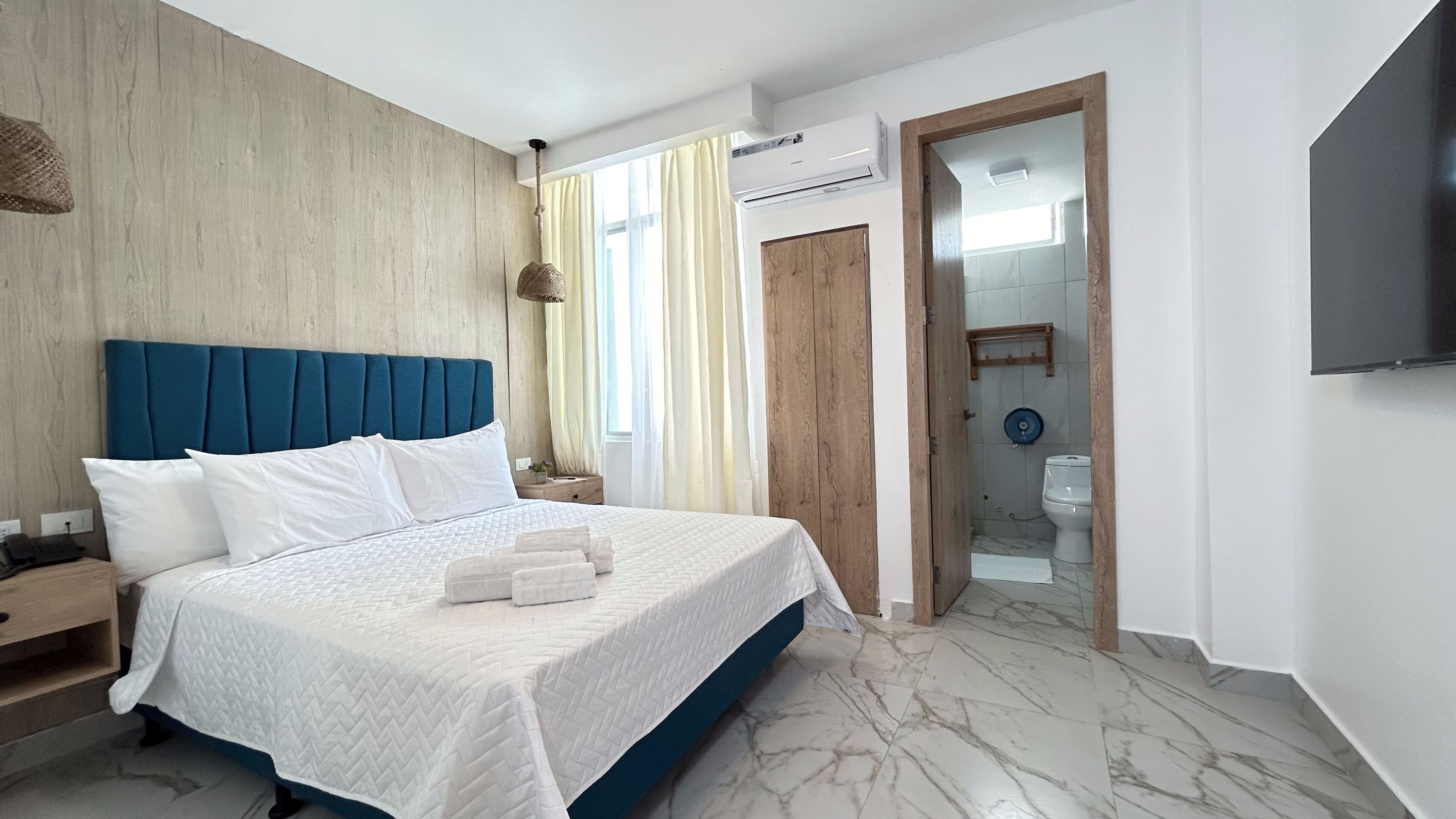 A modern bedroom with a large bed, wooden headboard, and a TV mounted on the wall.