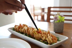 A white rectangular plate with a dish of breaded and fried food garnished with red and yellow peppers, served on a bed of greens.
