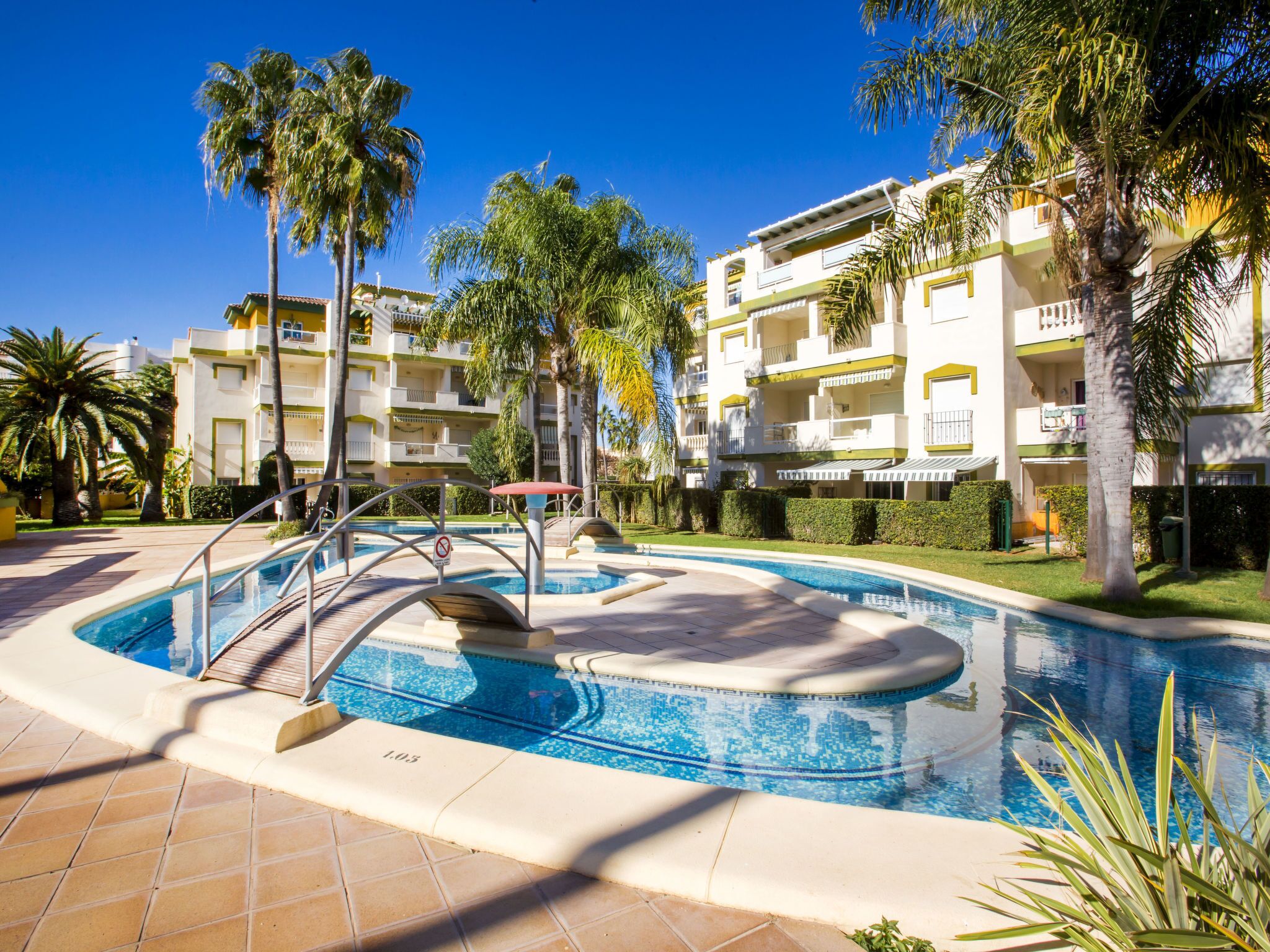 A swimming pool surrounded by palm trees and a multi-story building with balconies.