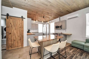 Une cuisine moderne avec un îlot central, des tabourets de bar blancs, une porte de grange en bois et un canapé vert.