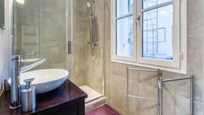 Ein modernes Badezimmer mit einer gläsernen Duschkabine, einem großen weißen Waschbecken und einem Fenster mit Aussicht.