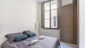 Ein Schlafzimmer mit Bett, Kissen, einem Nachttisch, einem Fenster und einer Tür.