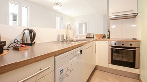 A modern kitchen with white cabinets, a dishwasher, an oven, and a wooden countertop. - Jardin Public | Bright & Stylish 1BR Apt for 4 Guests (Bordeaux)