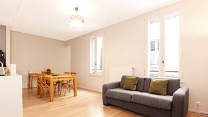 A spacious living area with a grey sofa, wooden dining table, and chairs. - Jardin Public | Bright & Stylish 1BR Apt for 4 Guests (Bordeaux)