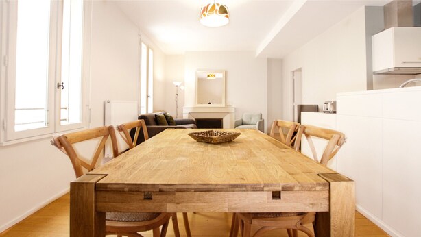 A dining room with a wooden table and chairs, a fireplace, and a view of the kitchen. - Jardin Public | Bright & Stylish 1BR Apt for 4 Guests (Bordeaux)