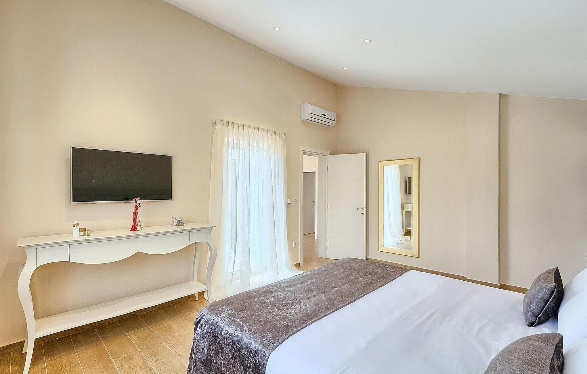 A hotel room with a bed, a TV, a vanity with a mirror, and a door leading to another room.