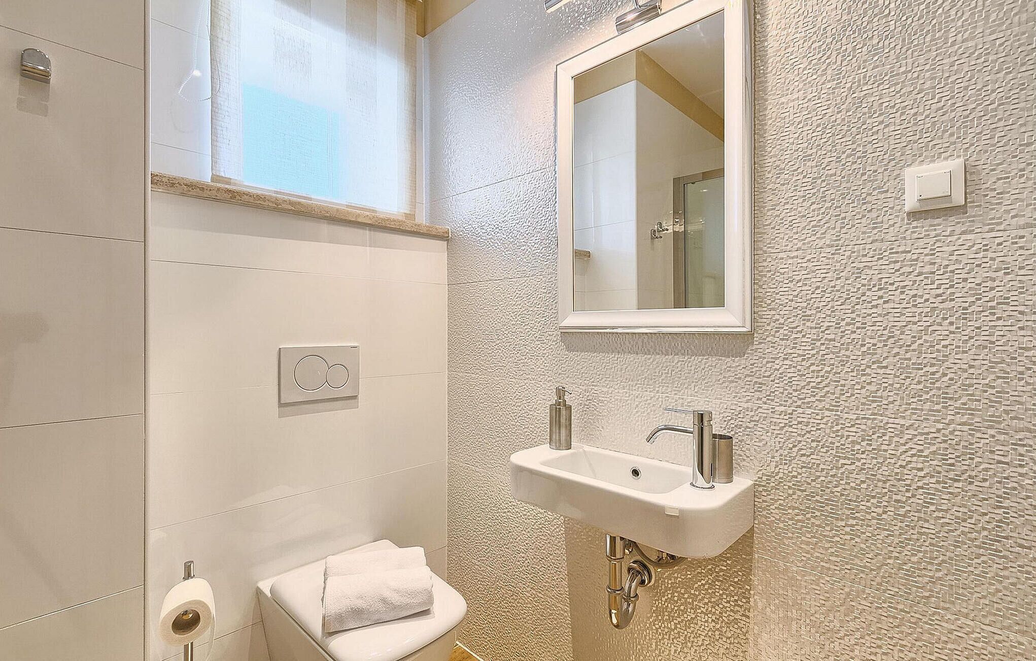 Une salle de bain avec un lavabo blanc, un miroir, une serviette et des toilettes.