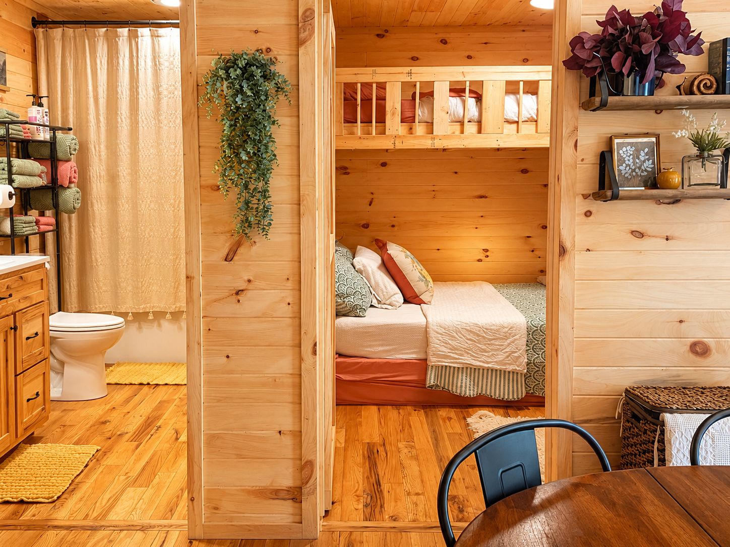 A wooden interior with a bunk bed, a toilet, a sink, and a dining area.