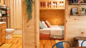 A wooden interior with a bunk bed, a toilet, a sink, and a dining area.