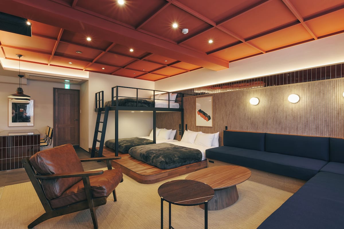 A modern hotel room with bunk beds, a sofa, a coffee table, and a dining area with chairs.