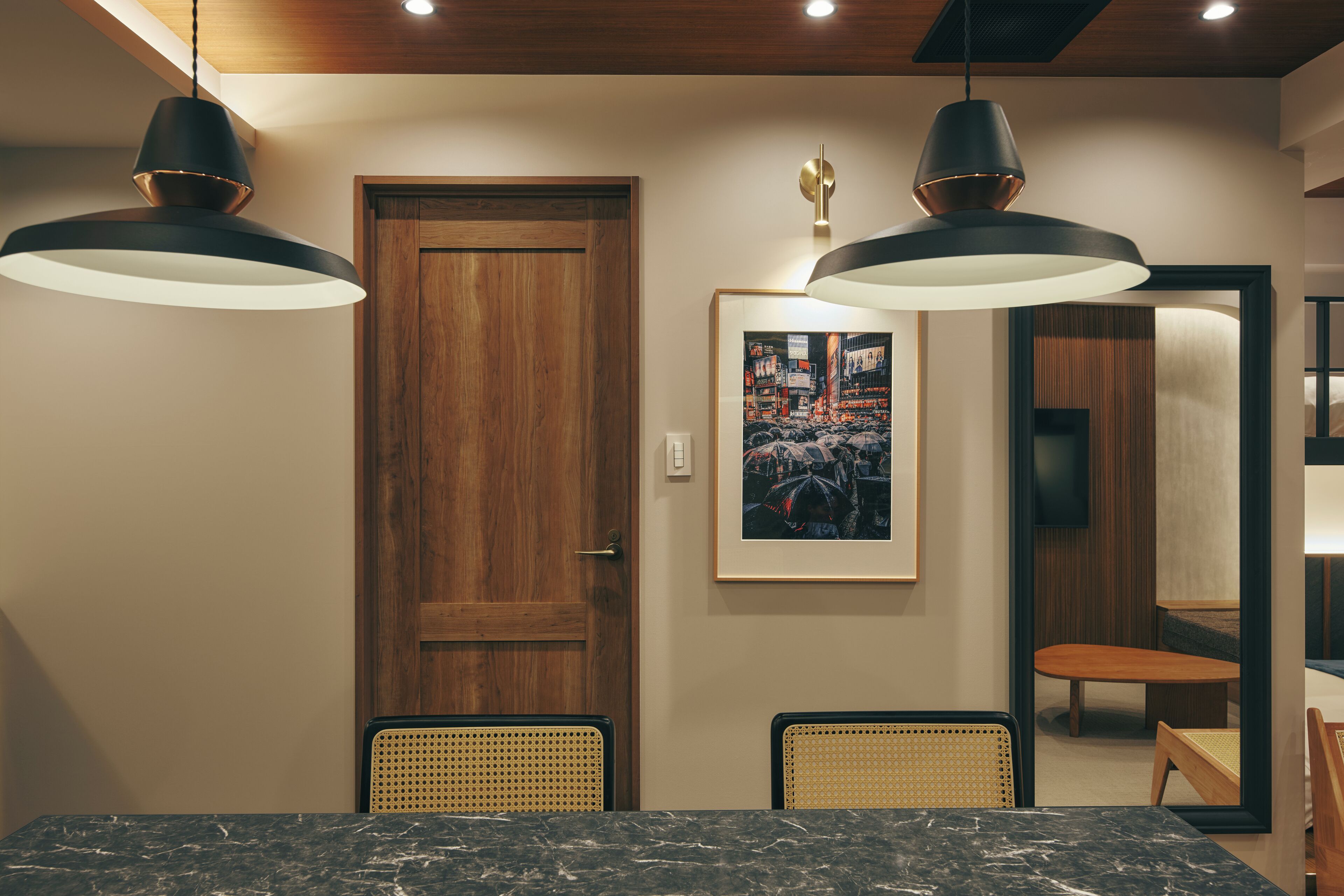 A dining area with a wooden door, two pendant lights, a framed picture, and a mirror reflecting the room.