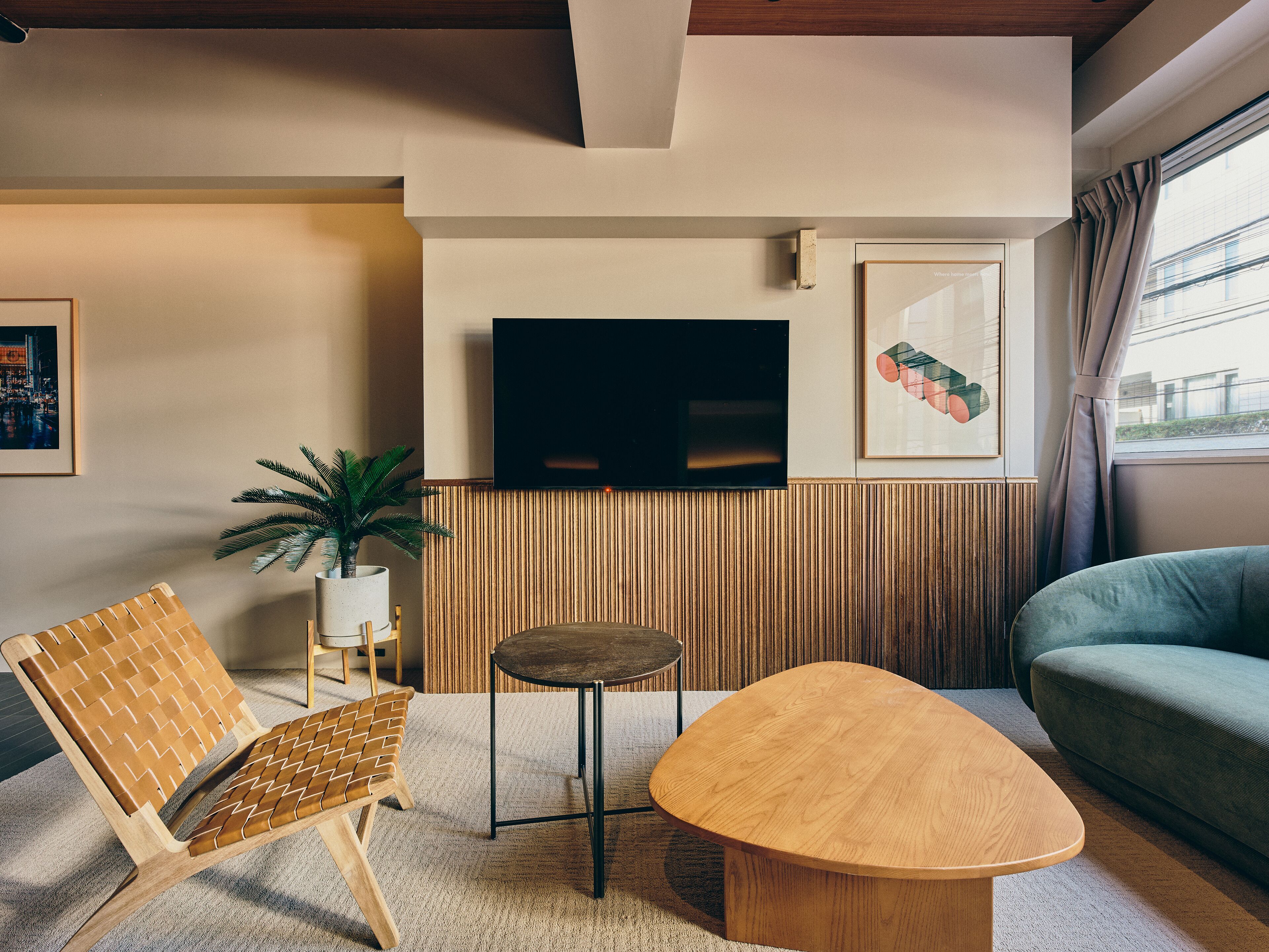 Una sala de estar moderna con una mesa de centro de madera, una silla de fibras naturales, una pequeña mesa redonda, una planta en maceta, un televisor de pantalla plana y una obra de arte enmarcada en la pared.