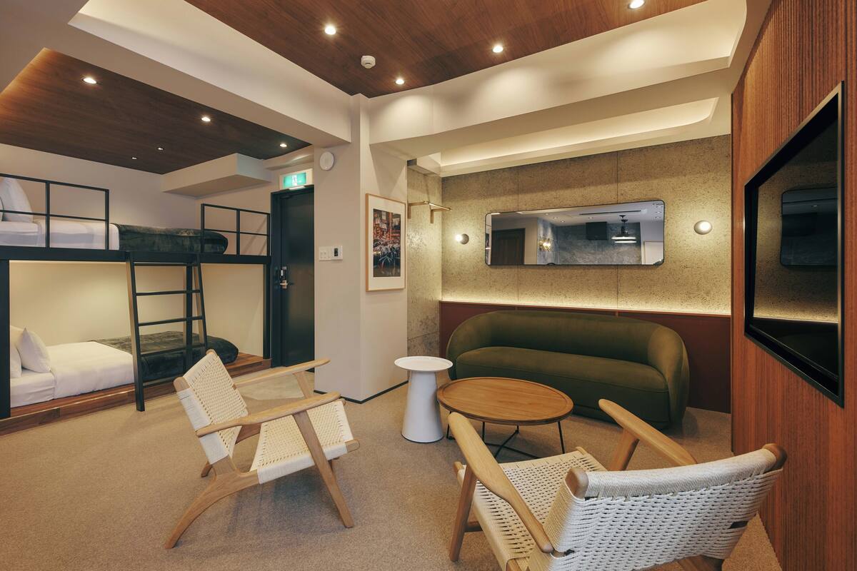 A modern hotel room with bunk beds, a sofa, a small round table, and wicker chairs.