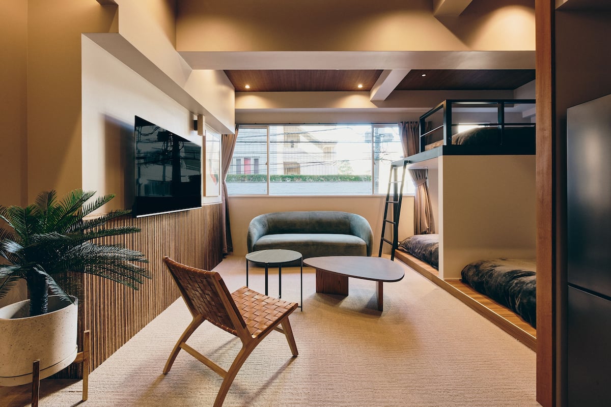 A compact living space with a sofa, a small round table, a TV mounted on the wall, and a potted plant.