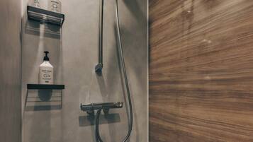 A modern shower with a handheld showerhead and a wall-mounted faucet. There are three bottles of toiletries on a shelf: body wash, shampoo, and treatment. The shower is adjacent to a wooden panel wall.