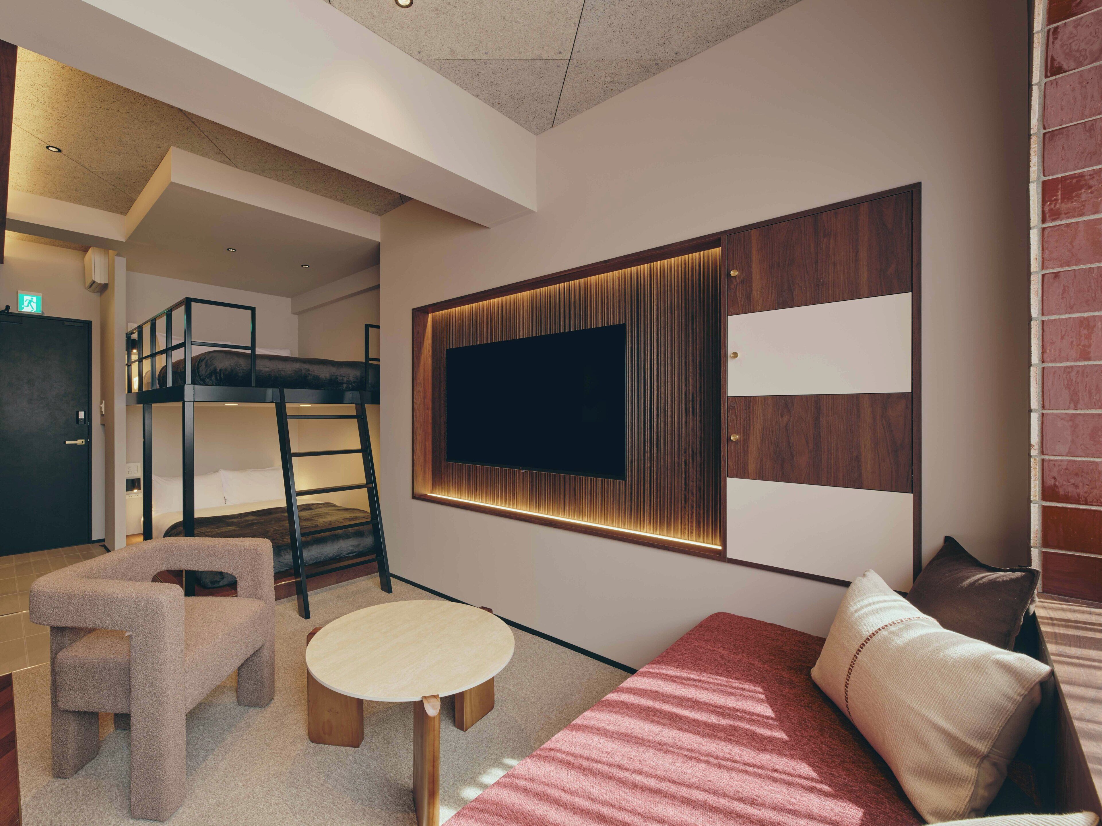 Una cama individual superpuesta, una mesa redonda, un sofá y un televisor montado en una pared con paneles de madera.