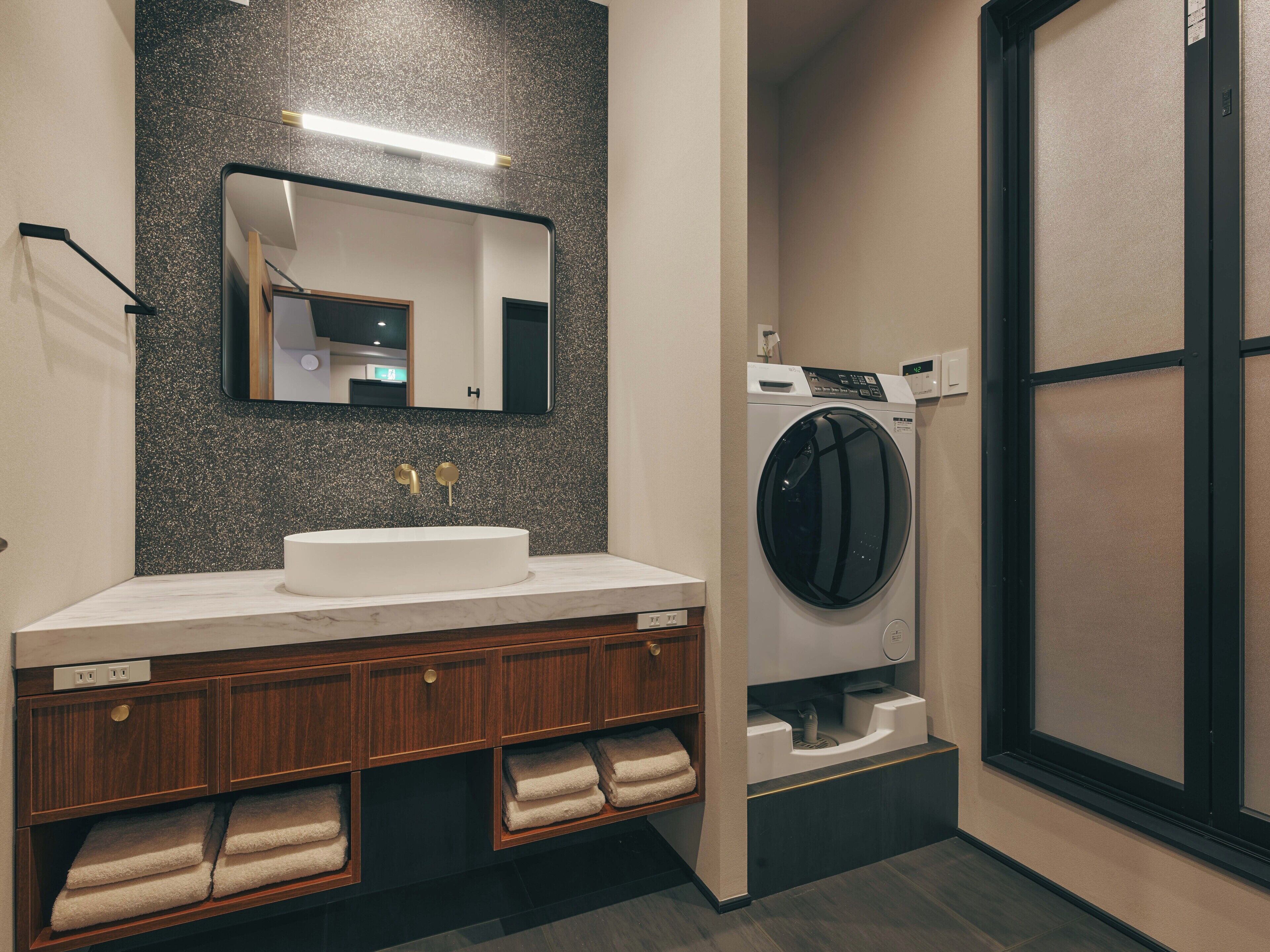 A modern bathroom with a white sink, a mirror, a washing machine, and wooden cabinets.