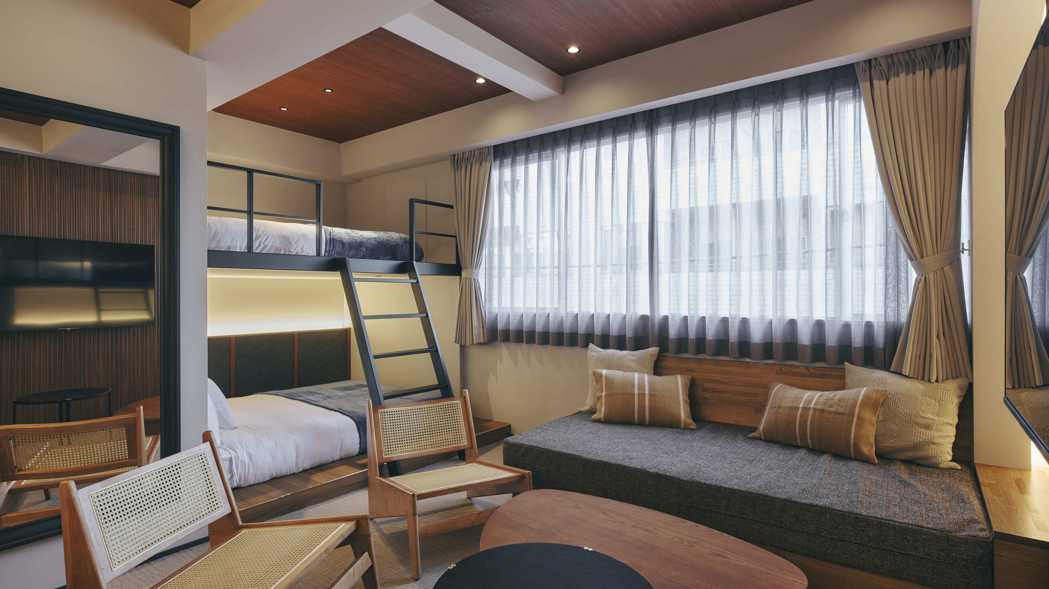 A bunk bed room with a ladder, a sofa, two chairs, and a window with curtains.