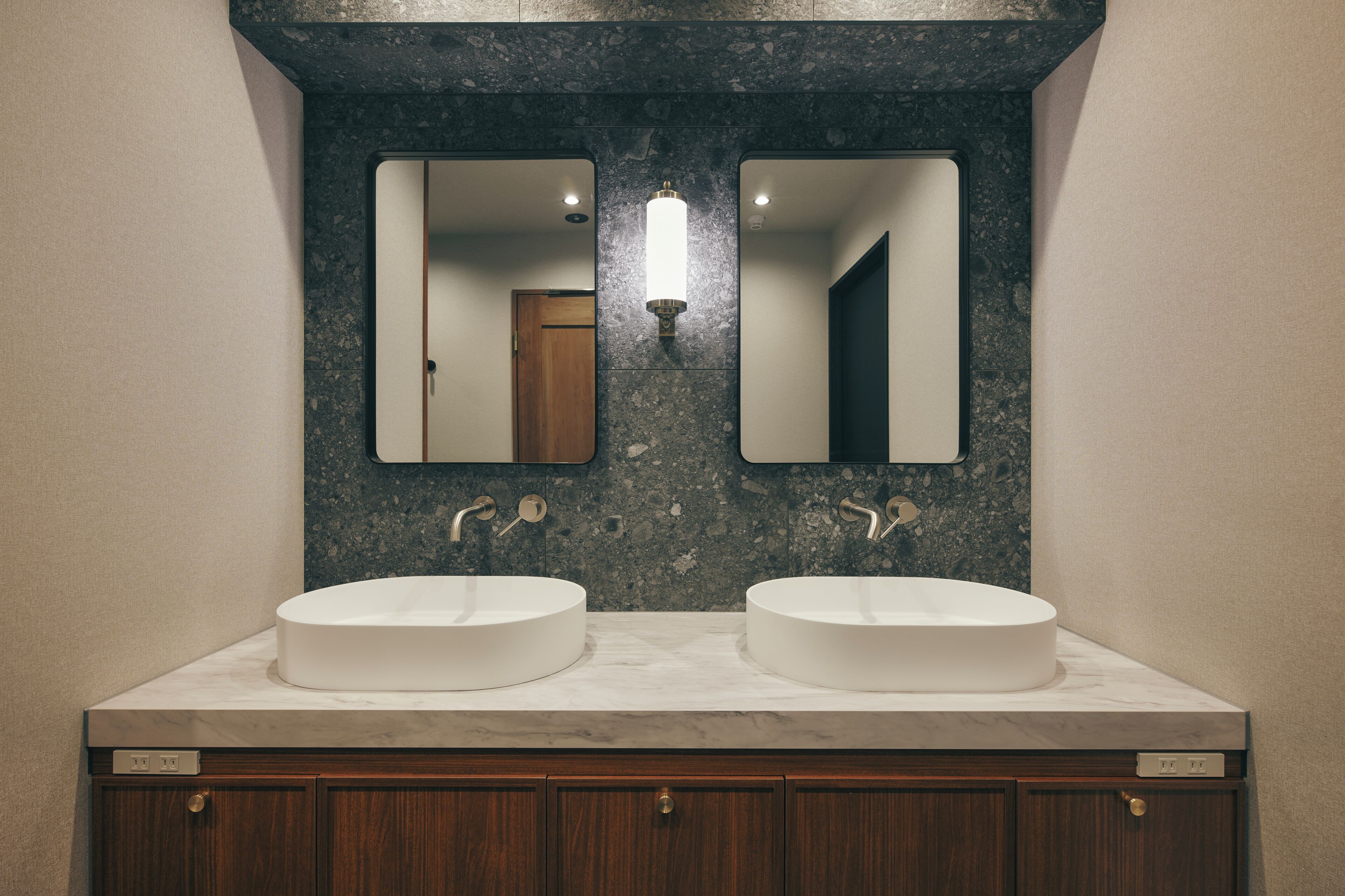 A bathroom with two sinks, a mirror, and a wall-mounted light fixture.