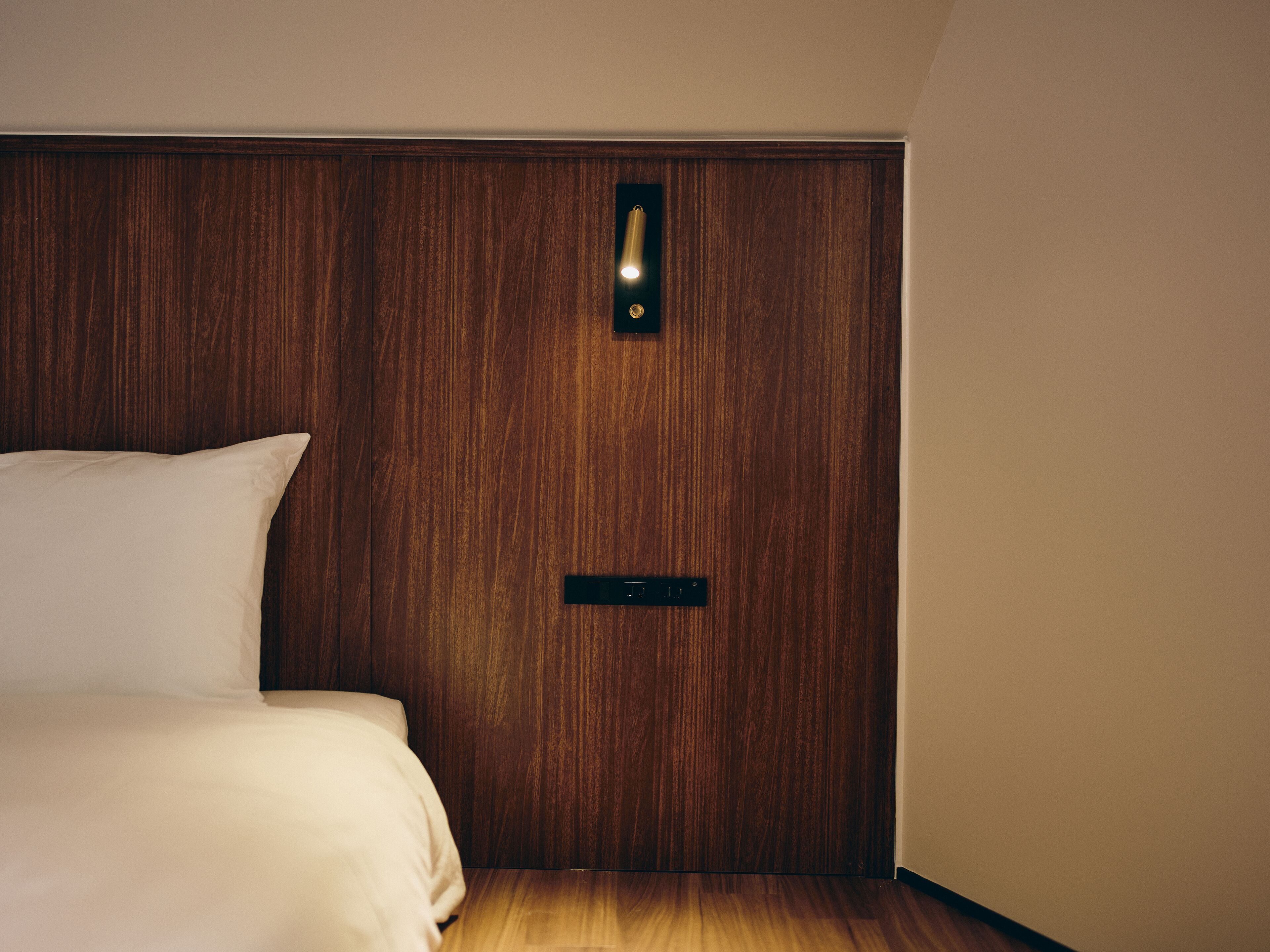 A bedroom with a wooden headboard, a bed with white bedding, and a nightstand with a black drawer.