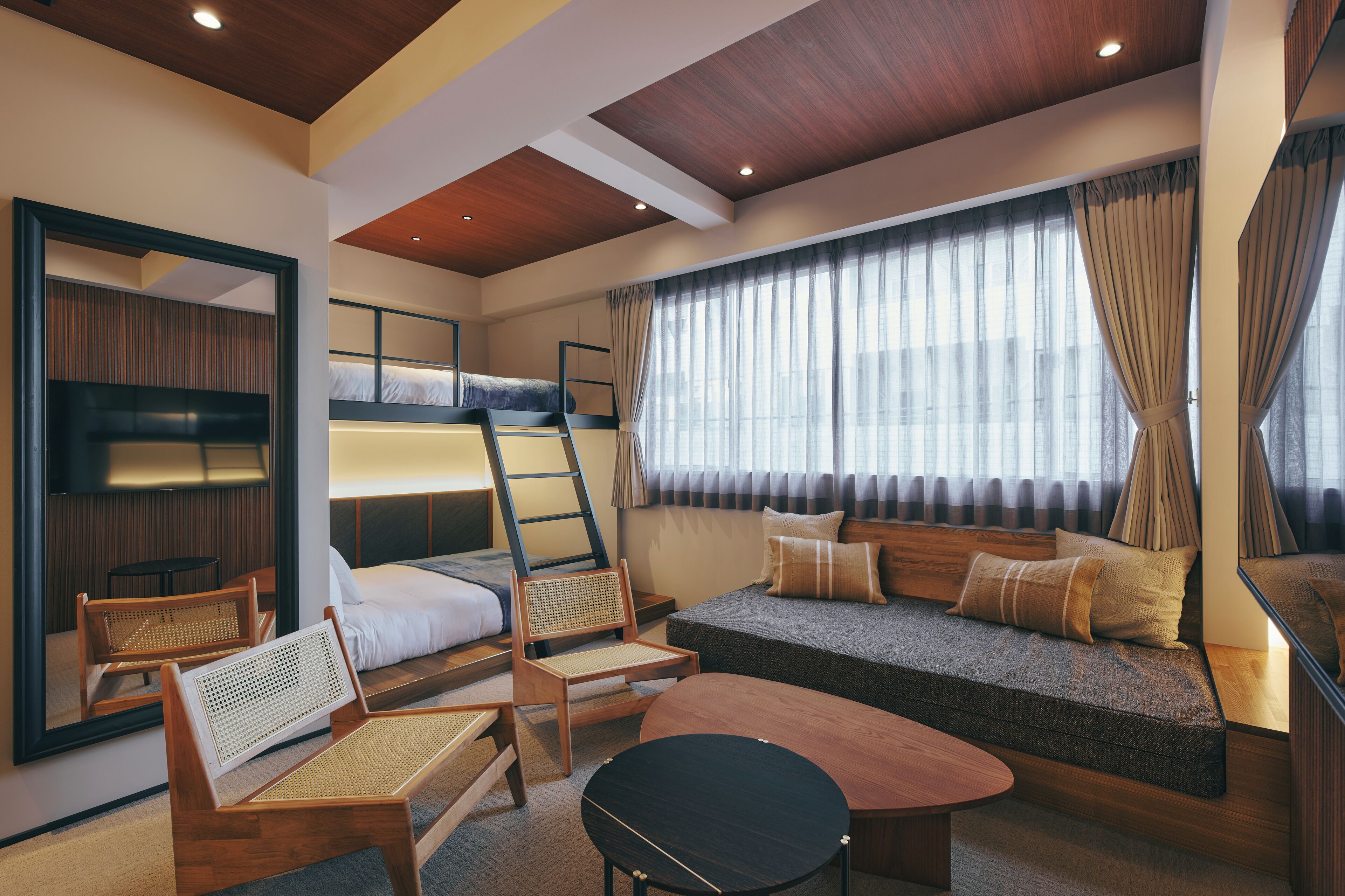 A modern hotel room with bunk beds, a sofa, a dining table, and a large window with curtains.