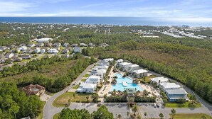 Vista aérea de una zona residencial con una gran piscina rodeada de casas, con vista despejada al océano y un camino que lleva al área de la piscina.