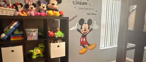 Una habitación con una estantería llena de juguetes y un vinilo decorativo de Mickey Mouse.