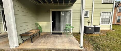 A covered patio area with a concrete floor, two green chairs, and a wooden table.