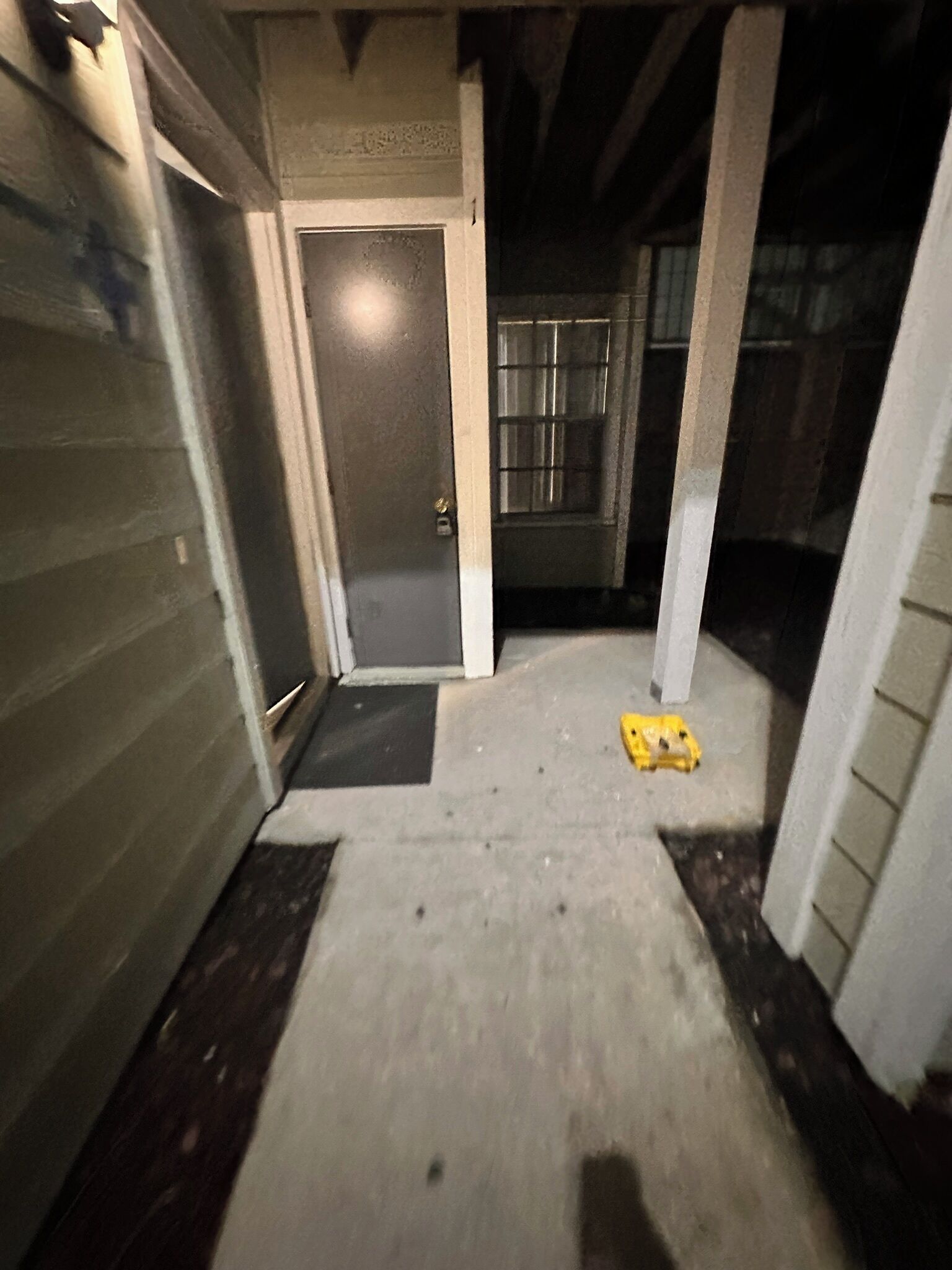 A narrow hallway with a door at the end, a concrete floor, and a yellow object on the ground.