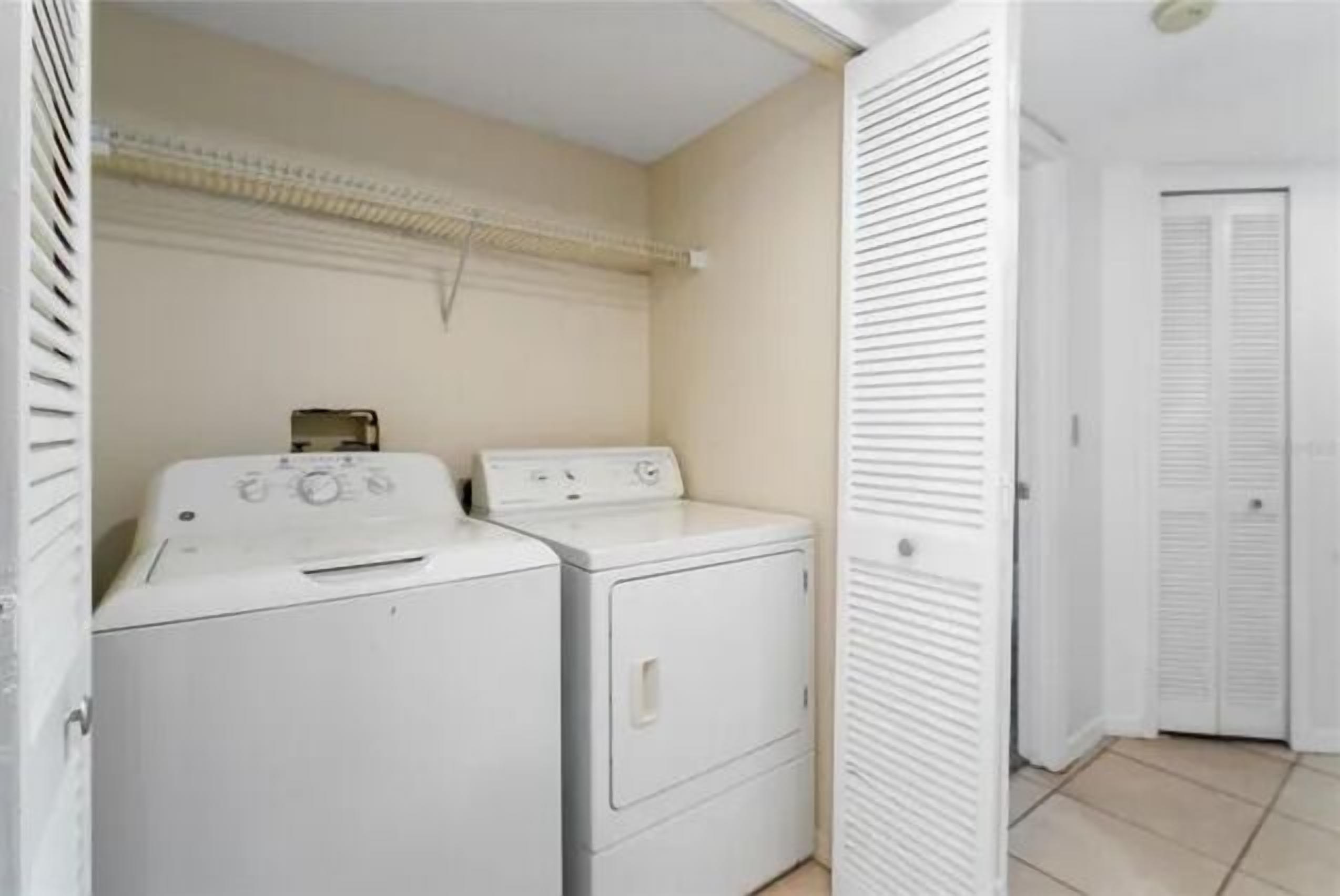 A laundry room with two stacked washing machines and a drying rack.